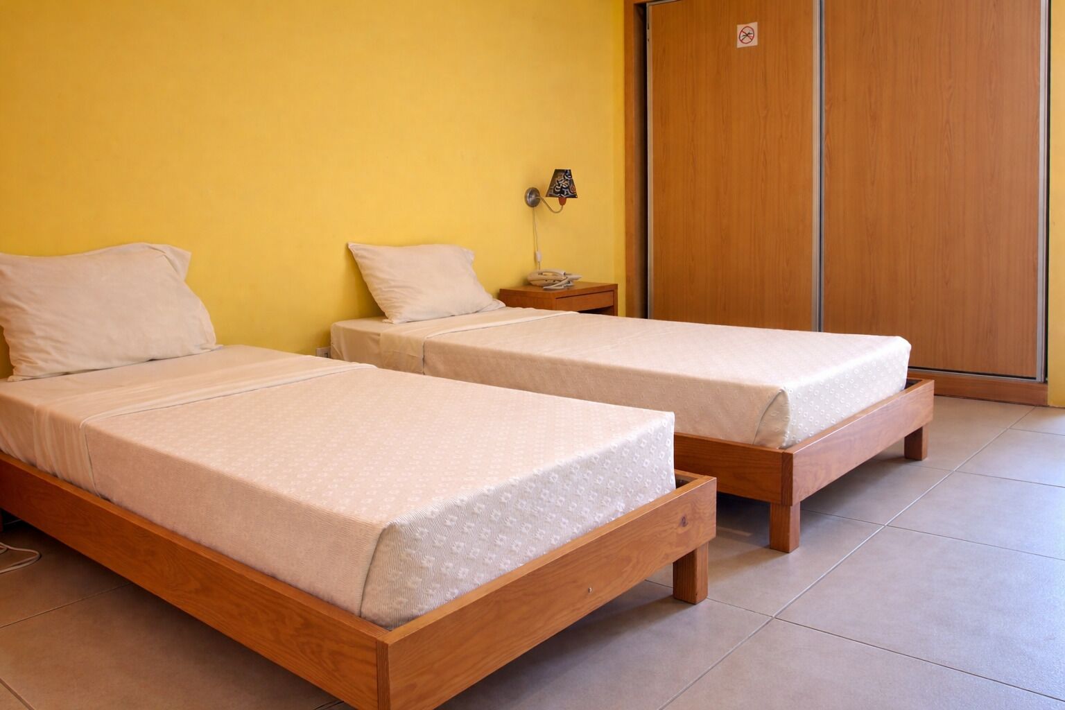 Two wooden beds with beige bedding in a room with yellow walls and a wooden wardrobe.