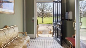 A hallway with a patterned floor, a chandelier, a sofa, and a door leading outside. - Stuart Suite (Edinburgh)