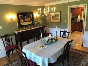 A dining room with a table set for six, surrounded by wooden chairs, a chandelier, wall sconces, and framed artwork.