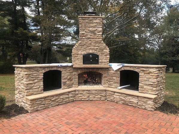 A stone-built outdoor fireplace with two chimneys, a plaque, and a brick-paved area.