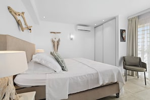 A modern bedroom with a bed, bedside lamp, air conditioning unit, and a chair. - oceanfront de luxe apartment Belair D, right on the ocean with private access (Kralendijk)