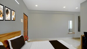 A hotel room with a large bed, a wooden headboard, a small table with a vase of flowers, and framed artwork on the wall. - Deluxehotel Chakripuram (Hyderabad)