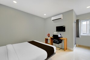 A modern hotel room with a bed, desk, chair, and air conditioning unit.