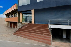 A building with a staircase leading to a glass entrance, a metal staircase on the ground floor, and a large blue shutter door.
