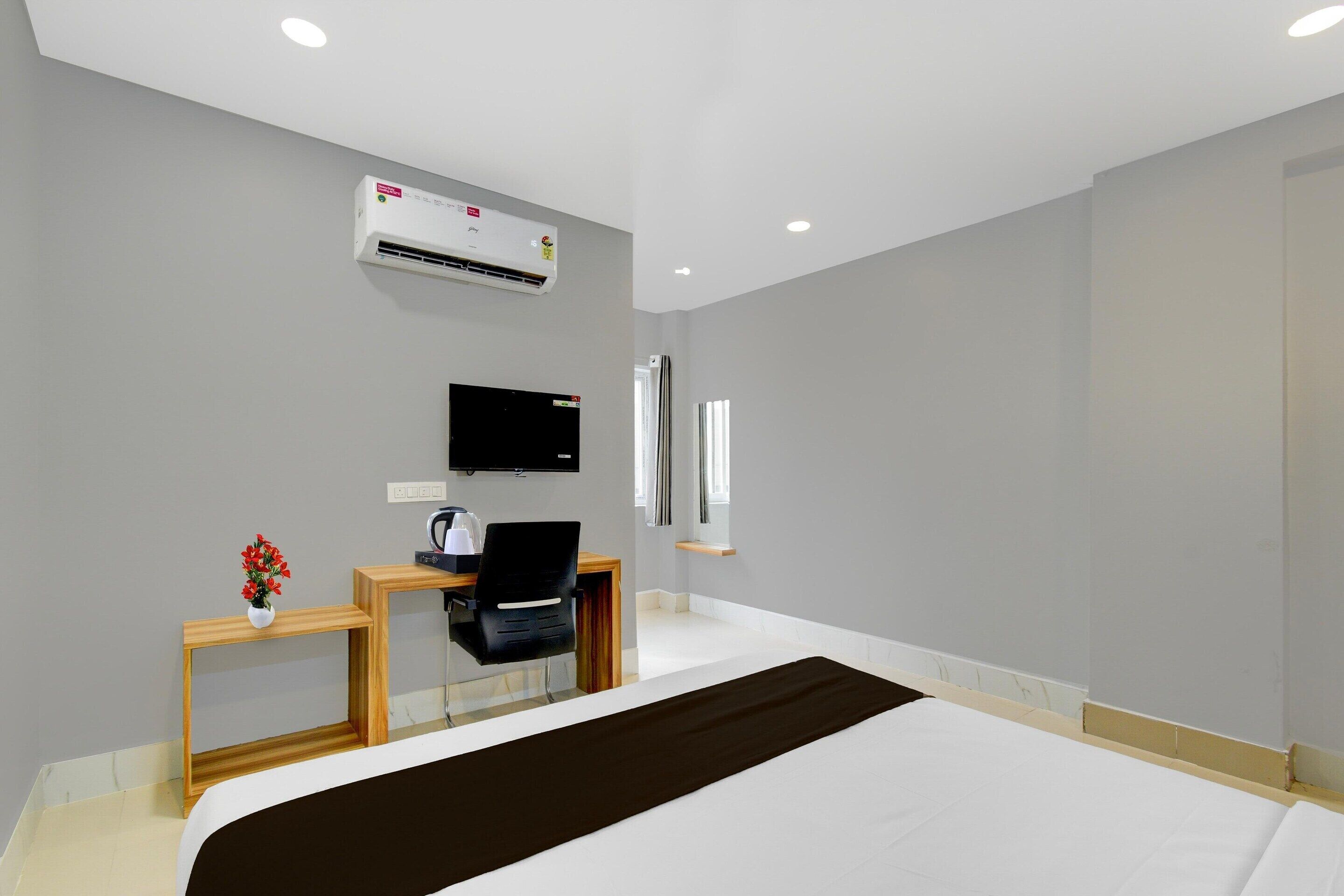 A hotel room with a bed, a desk with a chair, a television, an air conditioning unit, and a window.