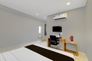 Habitació d'hotel amb un llit, escriptori amb cadira, televisió, aire condicionat i una petita planta.