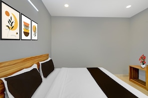Habitación de hotel moderna con una cama grande, cabecera de madera, mesita de noche con un jarrón de flores y tres cuadros abstractos enmarcados en la pared.