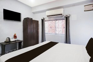 Habitación de hotel con cama, televisor de pantalla plana, armario, escritorio con tetera y tazas, y ventana con cortinas.