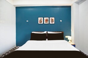 A hotel room with a blue accent wall, a bed with black and white bedding, and three framed botanical prints. - Deluxe Noonmati Guwahati Hotel Sundari (Guwahati)