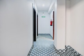 A hallway with a patterned floor, a fire exit sign, and a fire extinguisher. - Deluxe Noonmati Guwahati Hotel Sundari (Guwahati)