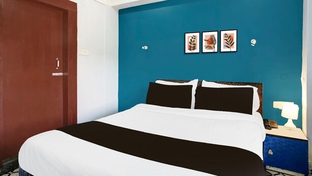 Ein Hotelzimmer mit einem Bett, einem Nachttisch, einer Lampe und drei gerahmten Blätter-Kunstwerken an der Wand.