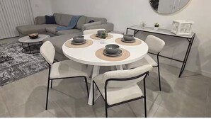 Un comedor con una mesa redonda, cuatro sillas y un sofá gris al fondo.