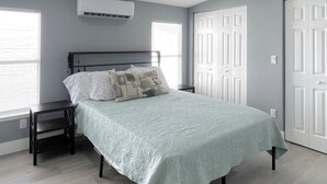 Een slaapkamer met een bed, nachtkastje, plafondventilator, airconditioning en een raam met jaloezieën.