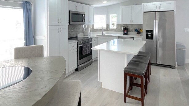 Een moderne keuken met witte kasten, een roestvrijstalen koelkast, een magnetron, en een groot eiland met zitplaatsen.