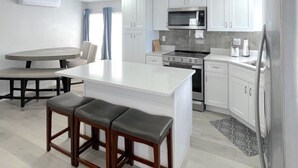 Een moderne keuken met witte kasten, een centraal eiland, een eethoek met een tafel en banken, en een inbouwmagnetron.