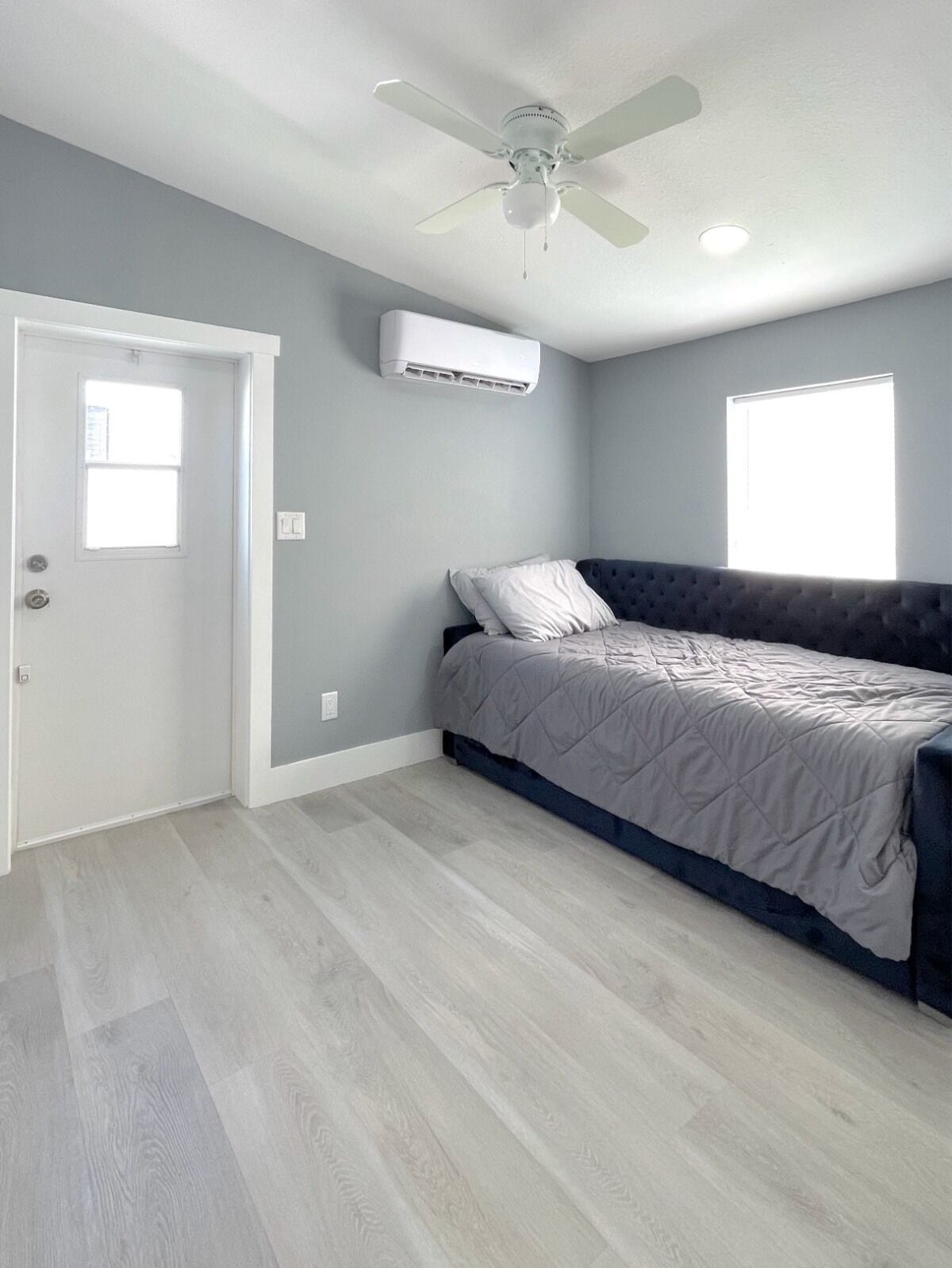 Un dormitorio con cama, ventilador de techo, aire acondicionado, una puerta y una ventana.