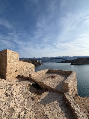 A stone fortification with a view of a bridge over water and distant mountains. - NEW-room with direct sea view-shared bathroom-all-in equipment- 2 pers. (Pag)