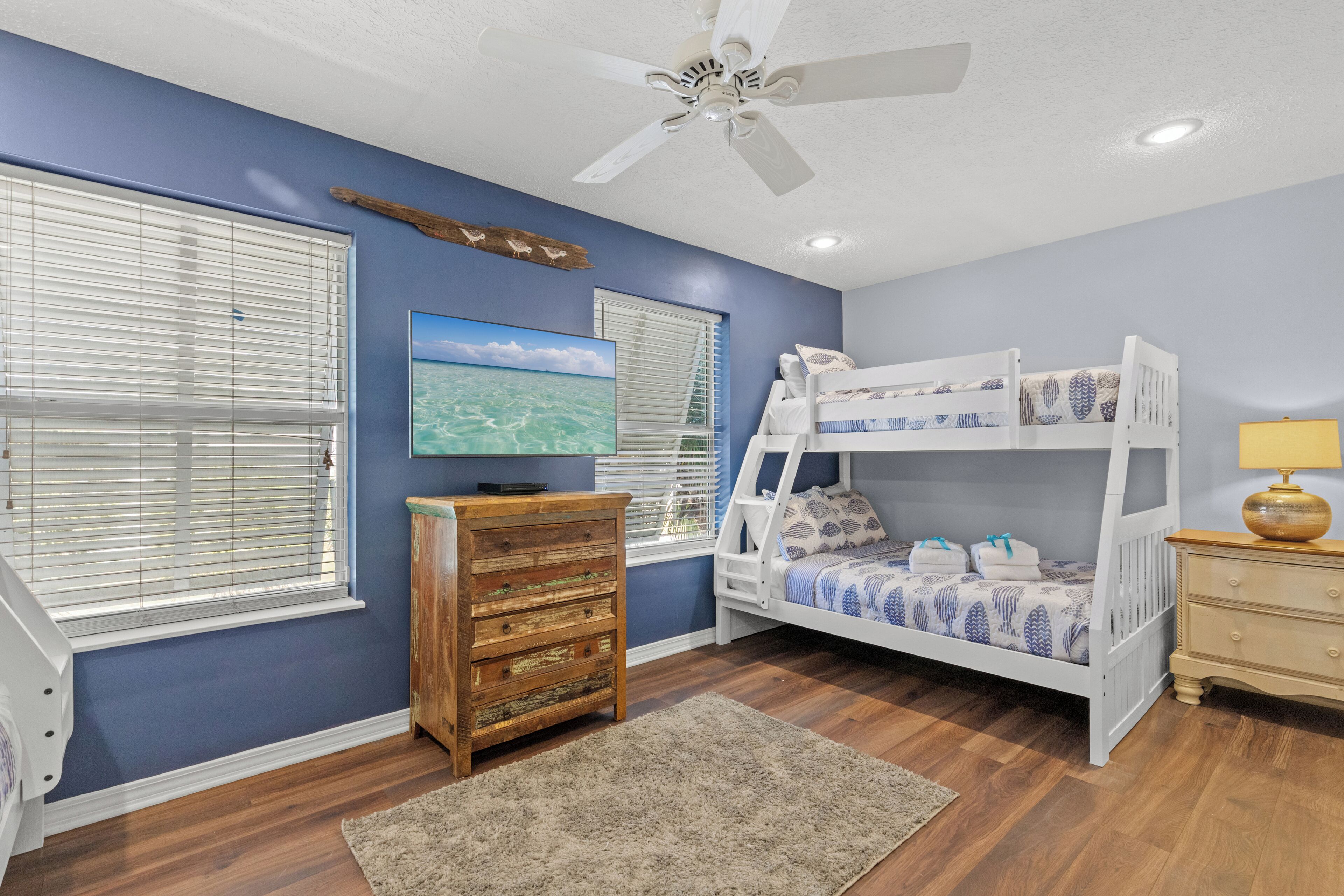 A bedroom with a bunk bed, wooden dresser, and a ceiling fan.