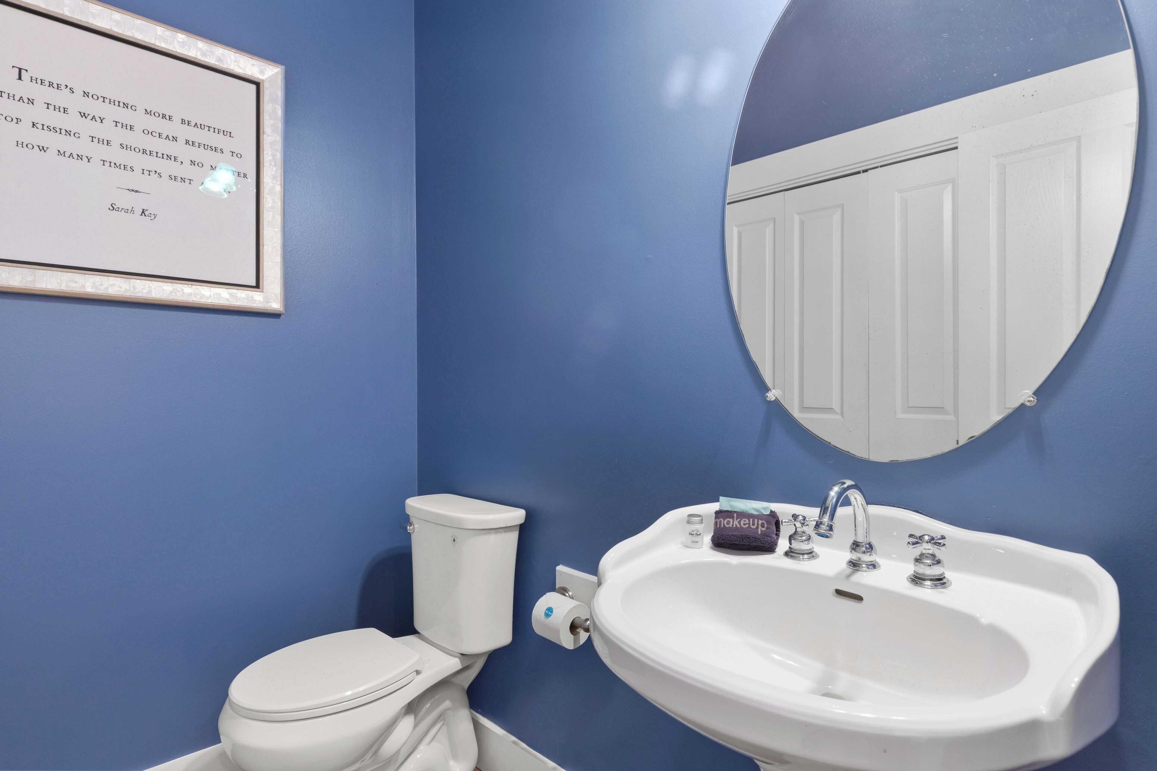 A bathroom with a toilet, sink, and a framed quote on the wall.
