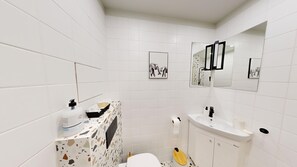 Een badkamer met witte tegels, een toilet, een wastafel, een spiegel en een foto van olifanten aan de muur.