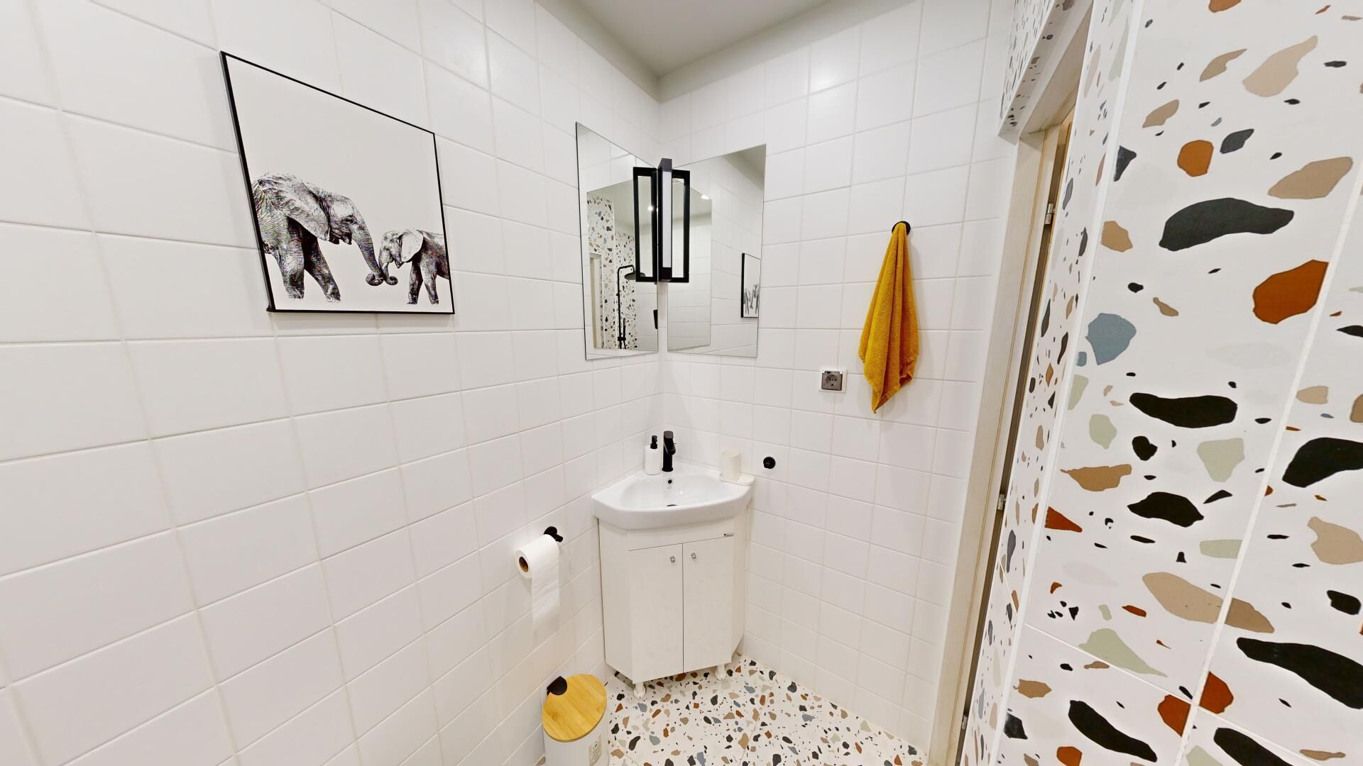 A bathroom with white tiled walls, a white sink, a mirror, and a shower curtain with a speckled pattern.