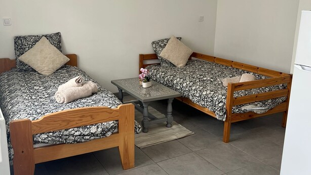 Ein kleines, sauberes Zimmer mit zwei Holzbetten, einem kleinen Tisch und einem weißen Kühlschrank.