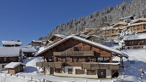 Eine Holzchalet mit einem Balkon, umgeben von schneebedeckten Bäumen und Gebäuden.