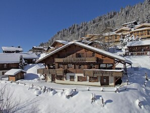 A wooden chalet with a balcony, surrounded by snow-covered trees and buildings. - Chalet, terrace, fireplace or stove, parking, 145m², Les Gets (Les Gets)