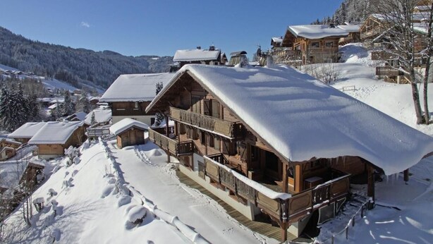 Eine Holzhütte mit schneebedecktem Dach, Holzbalkonen und Blick auf die verschneite Landschaft.