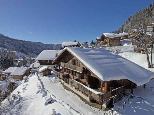 A wooden lodge with a snow-covered roof, wooden balconies, and a view of the surrounding snowy landscape. - Chalet, terrace, fireplace or stove, parking, 145m², Les Gets (Les Gets)