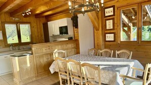 Ein rustikales Holzhaus-Interieur mit Esstisch, Stühlen, einer Chandelieber und einer Küchenzeile.
