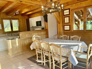 A wooden cabin interior with a dining table, chairs, a chandelier, and a kitchen area. - Chalet, terrace, fireplace or stove, parking, 145m², Les Gets (Les Gets)