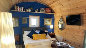 Una habitación acogedora con una cama, una lámpara, un televisor y una estantería con libros y una caja.