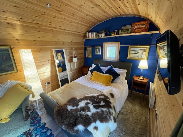 A cozy room with a bed, a mirror, a small table, and a wall-mounted TV.