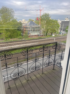 A balcony with a metal railing overlooking a railway track and a construction site with scaffolding.