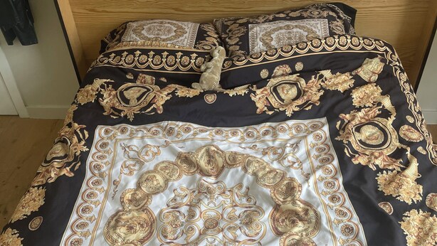Een bed met een decoratieve spreidek die gedetailleerde patronen en een medaillon in het midden heeft.