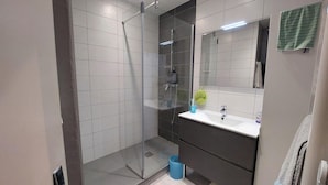Un baño moderno con cabina de ducha de vidrio, lavamanos blanco y espejo.
