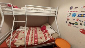 Habitación con literas, una manta estampada, una escalera y una pequeña silla naranja.