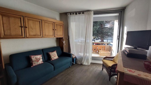 Una sala de estar con un sofá, un televisor y una ventana con cortinas.
