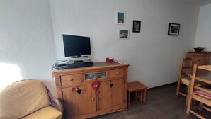 Una habitación con un armario de madera, un televisor, una mesita y una silla.