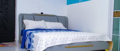 A bed with a white and blue patterned bedspread, a grey headboard, and a yellow bedside table.