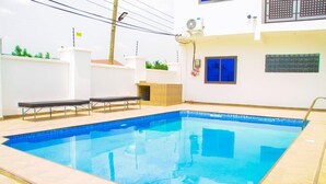 A swimming pool with a tiled deck, a bench, and a small structure with a tiled roof. - Lawson Guest house  (Kweiman)