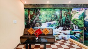 A room with a checkered floor, a brown leather sofa with red and orange cushions, and a black table with a vase of flowers. - Deluxeganakkal Near BGS Hospital Junction (Bengaluru)