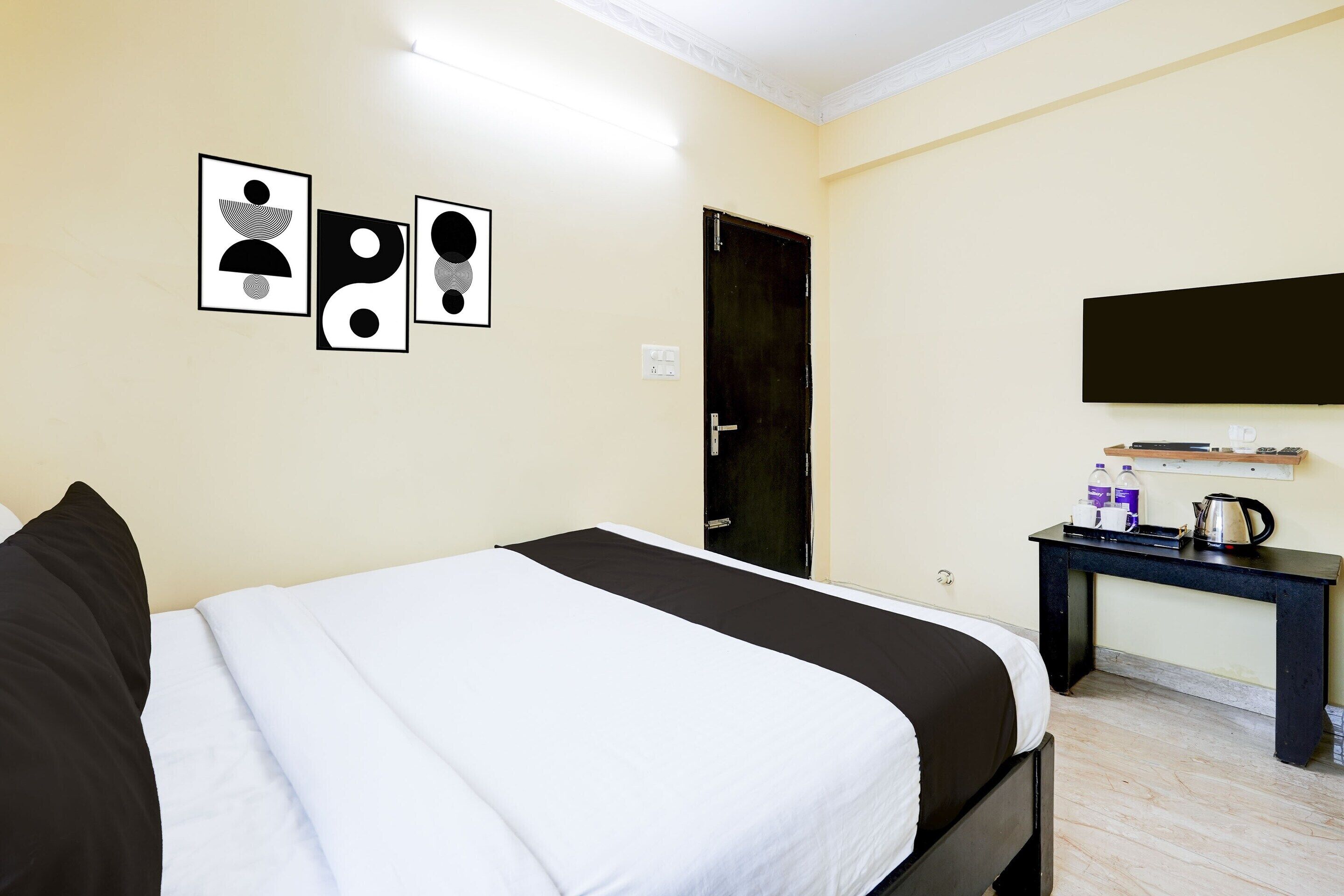 A hotel room with a bed, a desk with a flat-screen TV, a door, and wall art.