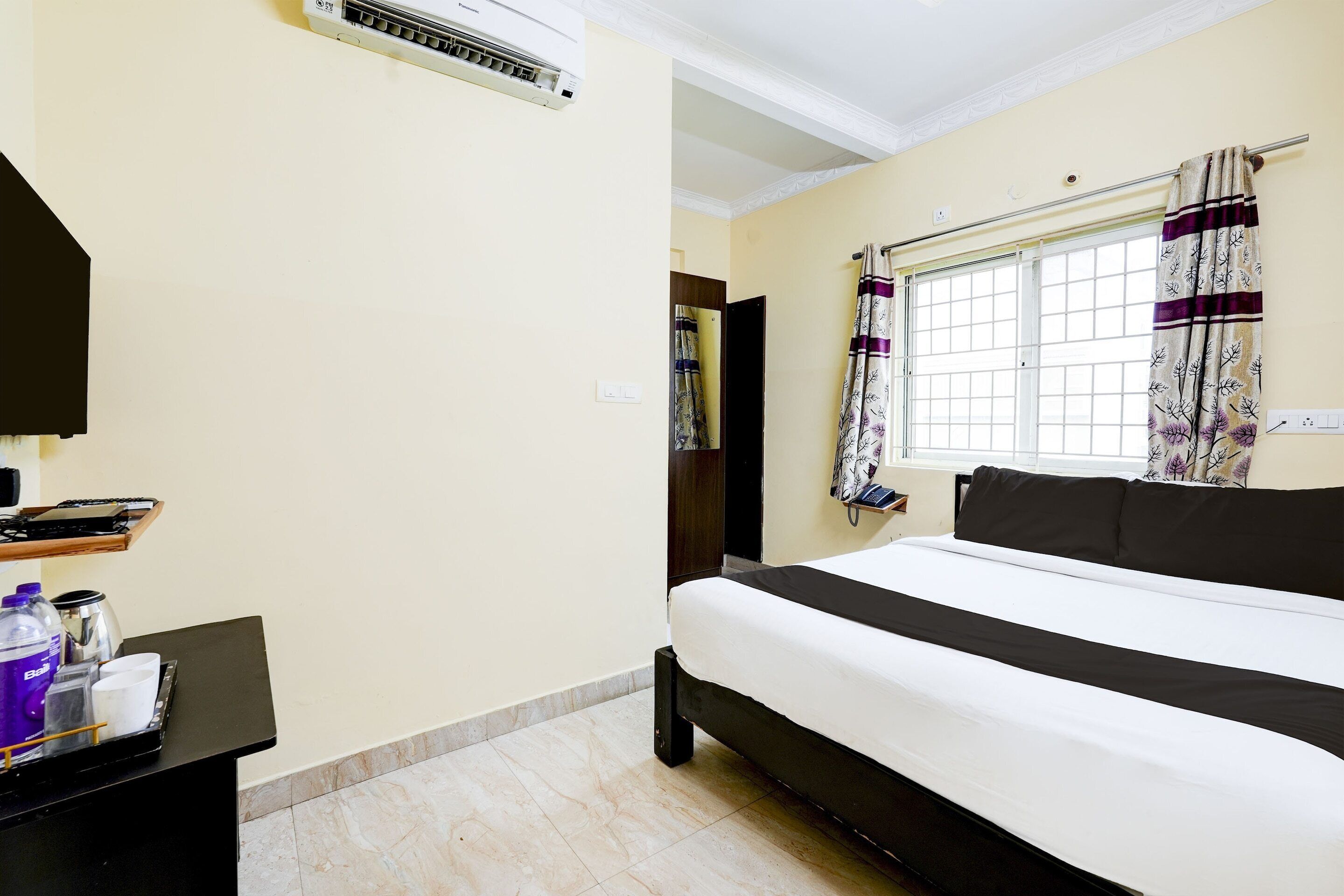 Habitación de hotel con cama, escritorio, teléfono, botella de agua y cafetera.