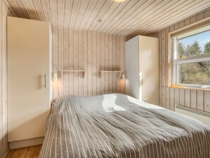 Une chambre à coucher avec un lit, des murs en bois, une fenêtre et des étagères intégrées.
