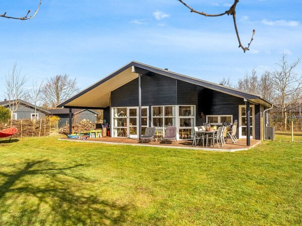 Une maison moderne dotée d’un patio couvert, de grandes fenêtres et d’une pelouse bien entretenue.