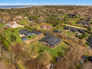 Vue aérienne d’un quartier résidentiel avec des maisons, une grande maison dotée d’un patio couvert, et une étendue d’eau en arrière-plan.