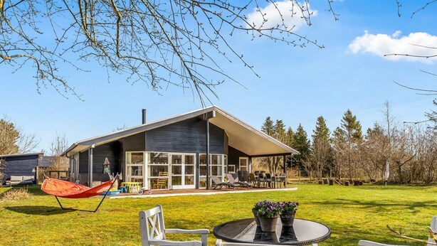 Une maison moderne dotée d’une grande terrasse, d’un espace salon extérieur et d’un hamac.