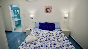 Un dormitorio con una cama, dos mesitas de noche, un armario y un aire acondicionado instalado en la pared, además se ve un baño a través de una puerta abierta.